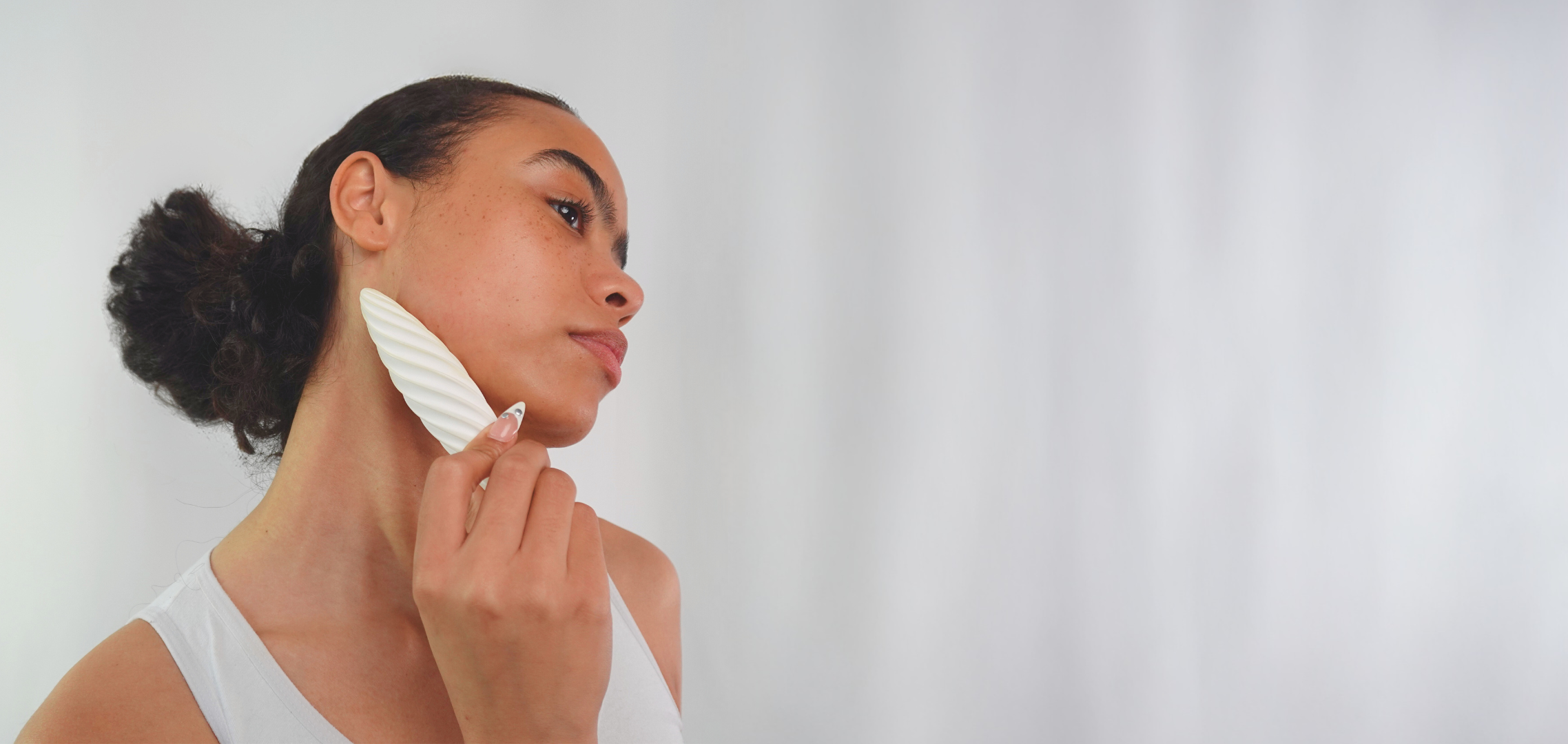 Bella gliding the white Fevowell Facer beneath her right chin to sculpt and lift the jawline during her skincare ritual